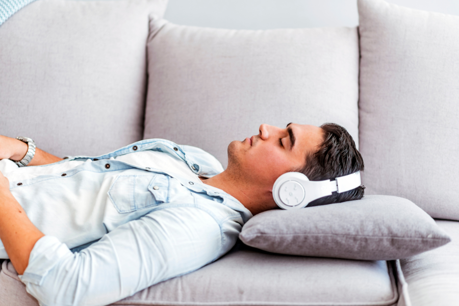Auditiver Lerntyp im Fernstudium: Mann liegt auf Sofa mit Kopfhörern auf den Ohren