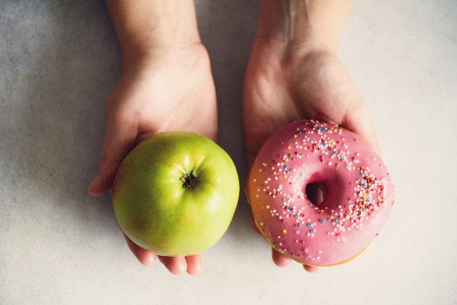 Zwei Hände, eine mit einem Apfel, die andere mit einem Donut. Die Qual der Wahl im MBA-Fernstudium.