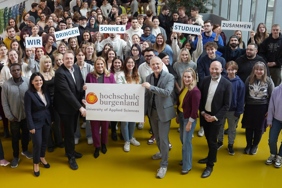 Schild mit neuem Logo und neuen Namen mit Geschäftsführer und Rektor, Mitarbeiter:innen und Studierenden der Hochschule Burgenland