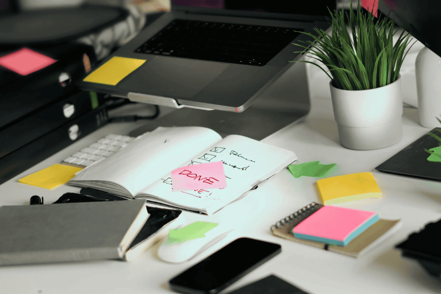 Schreibtisch mit Laptop, Kalender und Post-Its eines Studierenden im Fernstudium der neben dem Beruf sein Studium machbar macht.